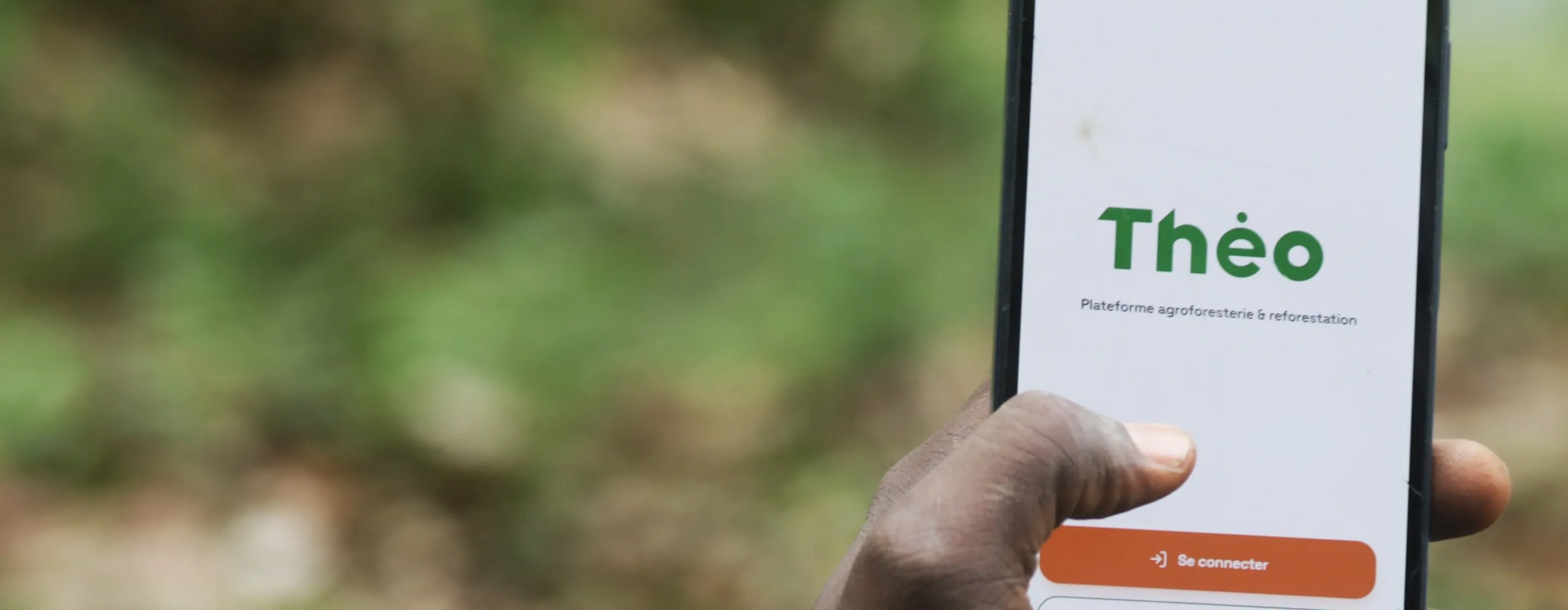 A hand holding a phone showing the home screen of the Theo app